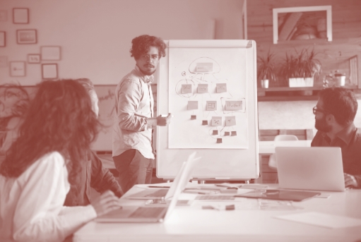 A imagem ilustra uma pessoa explicando com o auxílio de um quadro para outros indivíduos em uma reunião